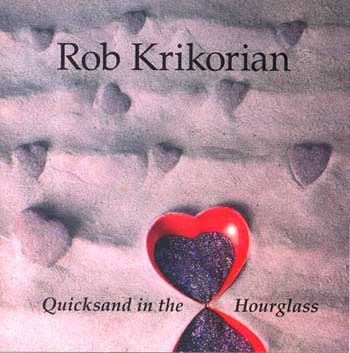 Quicksand in the Hourglass - CD front cover. Photo of an art object.  Two hearts, with points touching, form an hourglass which is lying on some sand.  The sand has several furrows, suggesting ocean waves.  In the background, numerous small hearts sink into the sand.